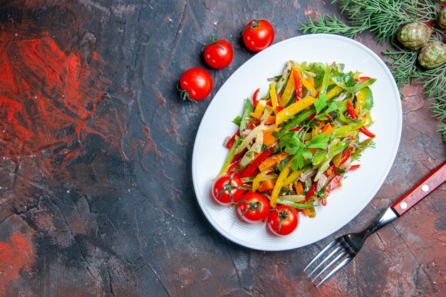 Vue de dessus salade de légumes sur plaque ovale fourchette de tomates cerises sur table rouge foncé copy space