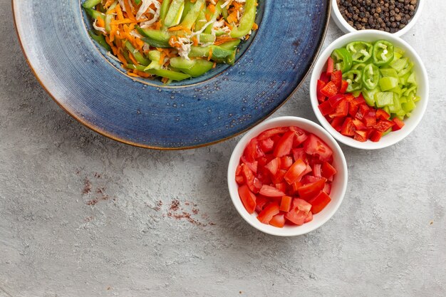 Vue de dessus salade de légumes en tranches avec assaisonnements sur fond blanc