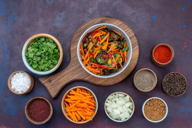 Vue de dessus salade de légumes en tranches à l'intérieur de la plaque avec des assaisonnements verts sur le bureau sombre