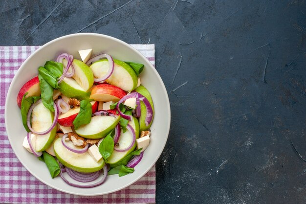 Vue de dessus de la salade de pommes dans un bol de serviette à carreaux violet et blanc sur une table sombre avec lieu de copie
