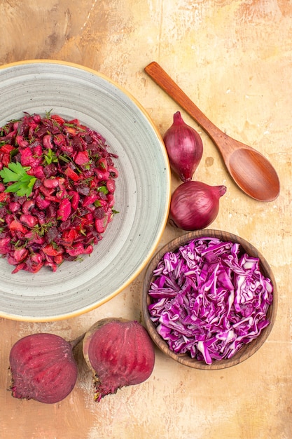 Vue de dessus de la salade saine rouge sur une assiette avec des feuilles de persil sur le dessus avec deux betteraves rouges d'oignons et un bol de chou haché sur un fond en bois