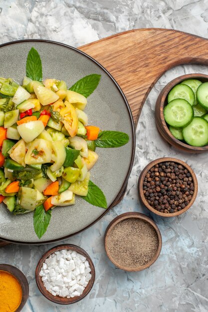 Vue de dessus salade de tomates vertes sur plaque ovale différentes épices dans des bols sur fond sombre