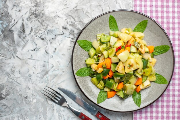 Vue de dessus salade de tomates vertes sur une plaque ovale fourchette de nappe rose sur une surface grise