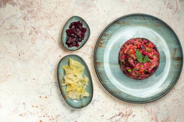 Vue de dessus de la salade de vinaigrette sur une assiette ovale de betteraves coupées et d'autres trucs dans des bols sur un espace libre de table gris clair