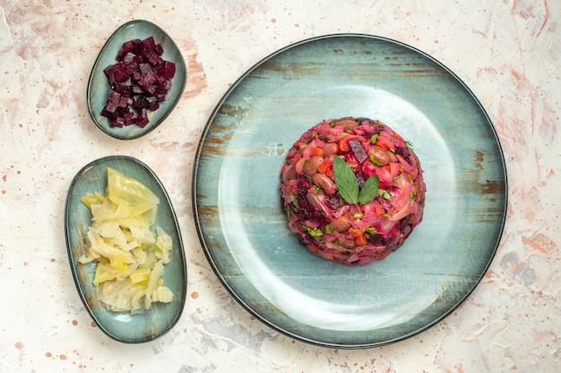 Photo gratuite vue de dessus de la salade de vinaigrette sur une assiette ovale de betteraves coupées et d'autres trucs dans des bols sur une table gris clair