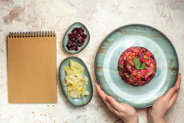 Vue de dessus de la salade de vinaigrette sur une assiette ovale dans des betteraves coupées à la main et d'autres trucs dans des bols sur une table gris clair