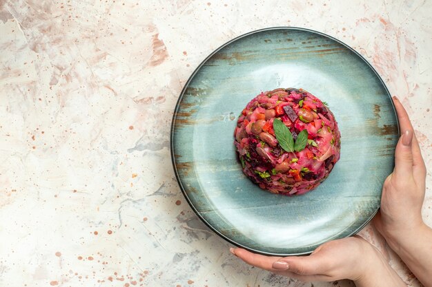 Vue de dessus de la salade de vinaigrette sur une assiette ovale dans une main féminine sur un espace libre de table gris clair