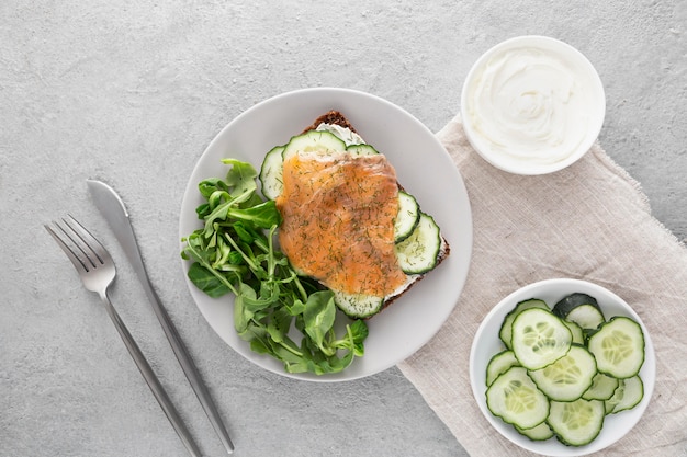 Vue de dessus sandwich avec concombres et saumon sur assiette avec couverts