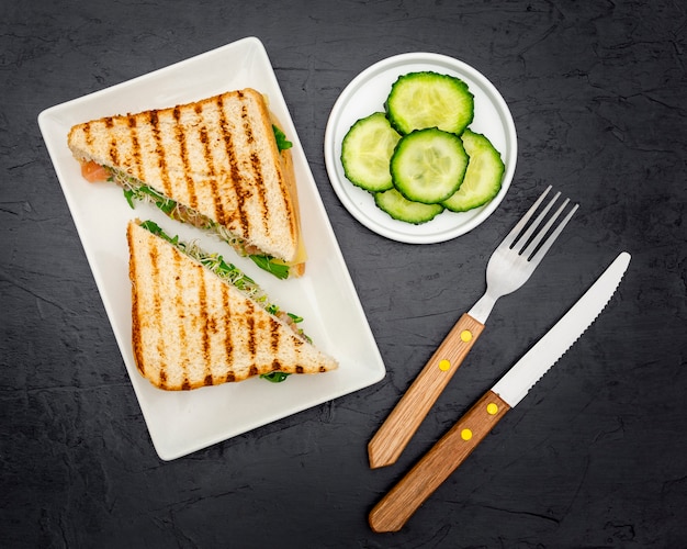 Vue de dessus des sandwichs triangulaires sur une assiette avec des couverts et des tranches de concombre