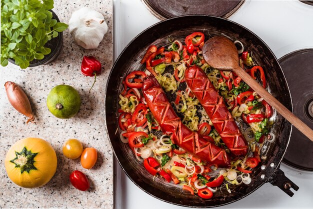 Vue de dessus des saucisses et mélange de légumes frits dans la poêle rustique