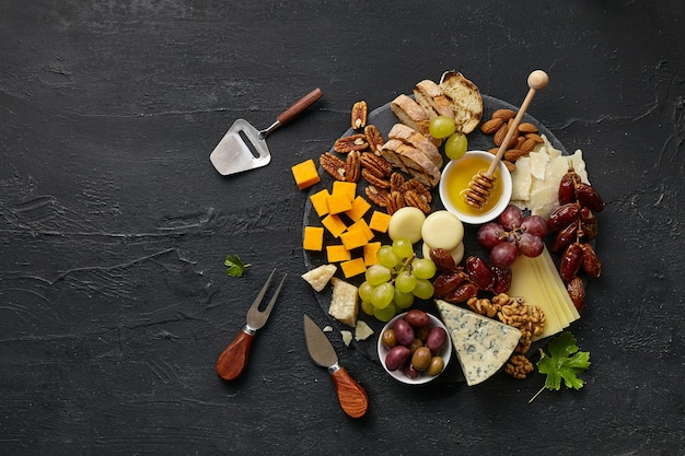 Vue de dessus d'une savoureuse assiette de fromages avec fruits, raisins, noix et miel sur une assiette de cuisine en cercle sur fond noir en pierre, vue de dessus, espace de copie. Nourriture et boisson gastronomiques.