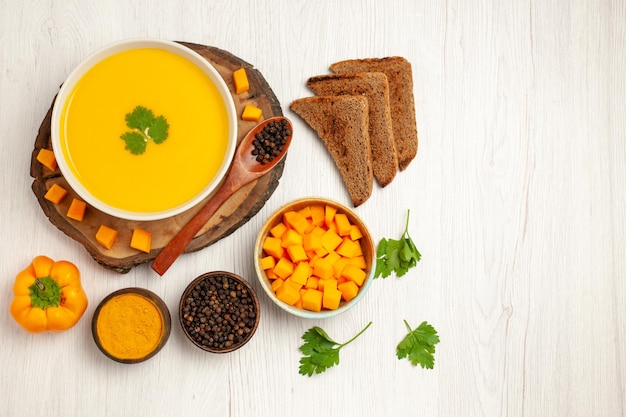 Vue de dessus d'une savoureuse crème de soupe à la citrouille texturée avec des miches de pain noir sur un tableau blanc