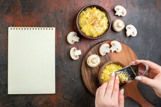 Vue de dessus savoureuse julienne dans un bol de champignons crus mains de femme râpant le cahier de mosarella sur une table marron