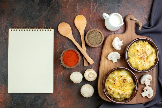 Vue de dessus savoureuse julienne dans des bols sur une planche à découper des cuillères en bois épices dans de petits bols cahier de champignons sur marron