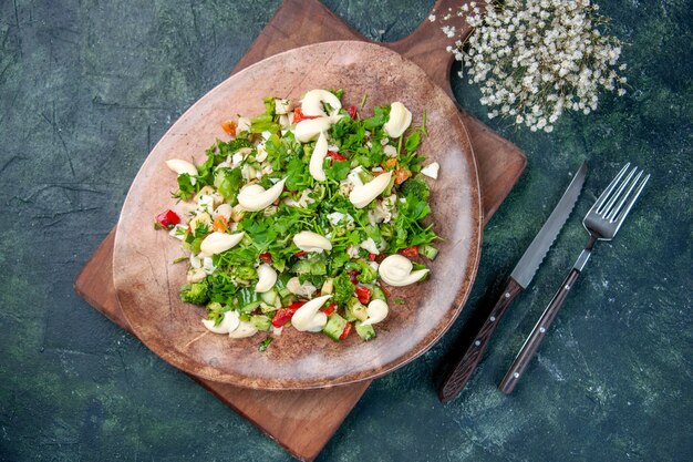 Vue de dessus savoureuse salade de légumes à l'intérieur de la plaque avec des couverts sur fond bleu foncé cuisine couleur santé ajustement dîner cuisine diète déjeuner repas restaurant