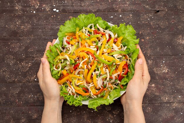 Vue de dessus savoureuse salade de légumes avec des légumes en tranches et salade verte à l'intérieur de la plaque ronde sur brun, repas alimentaire salade de légumes