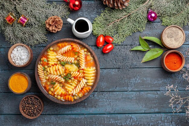 Vue de dessus savoureuse soupe de pâtes à partir de pâtes italiennes en spirale avec assaisonnements sur un bureau rustique bleu foncé soupe repas plat de couleur pâtes