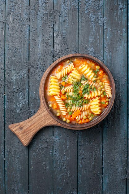 Vue de dessus savoureuse soupe de pâtes à partir de pâtes italiennes en spirale avec des verts sur un plat de cuisine de bureau bleu foncé soupe de couleur de pâtes italiennes