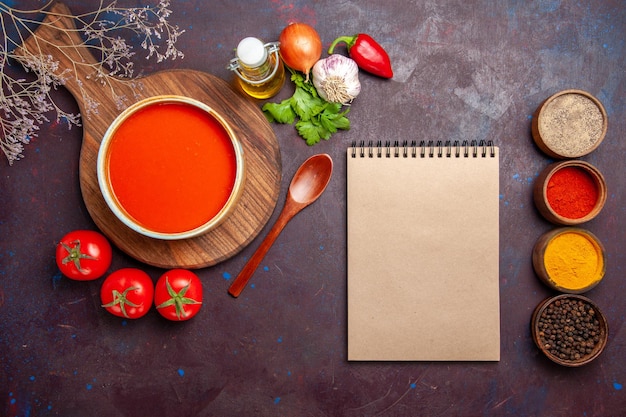 Vue de dessus d'une savoureuse soupe de tomates avec des assaisonnements et des tomates fraîches sur une table sombre