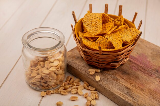 Vue de dessus de savoureuses chips croustillantes et épicées sur un seau sur une planche de cuisine en bois avec des pignons de pin sur un bocal en verre sur une table en bois beige