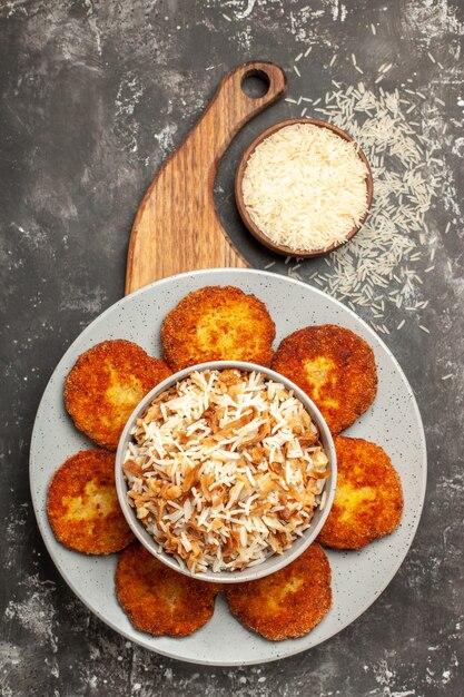 Vue de dessus de savoureuses côtelettes frites avec du riz cuit sur un plat de rissole de viande de bureau sombre