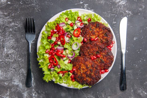 Vue de dessus de savoureuses côtelettes de viande avec salade fraîche sur fond gris photo plat de viande nourriture