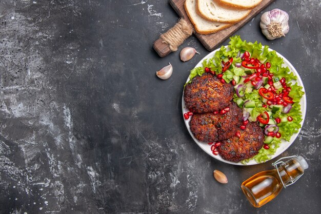 Vue de dessus de savoureuses côtelettes de viande avec salade de légumes sur plat de bureau gris repas photo