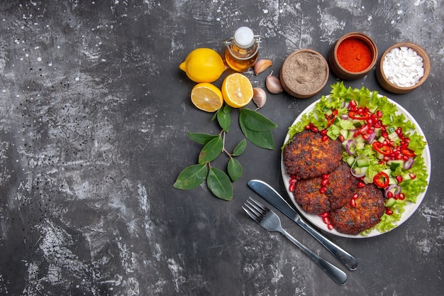 Vue de dessus de savoureuses côtelettes de viande avec salade de légumes sur plat de repas photo bureau gris