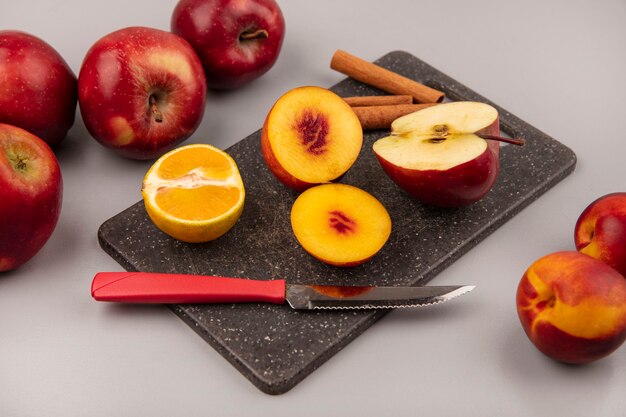 Vue de dessus de savoureuses demi-pêches sur un plateau de cuisine noir avec pomme mandarine et bâtons de cannelle avec couteau sur fond gris