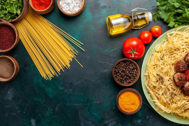 Vue de dessus de savoureuses pâtes italiennes avec des boulettes de viande et différents assaisonnements sur le bureau bleu foncé