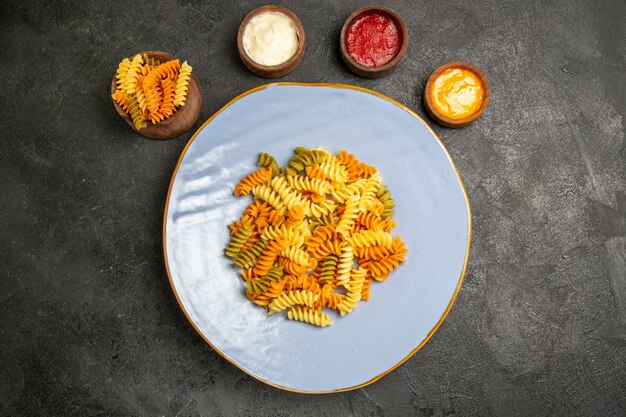 Vue de dessus de savoureuses pâtes italiennes pâtes en spirale cuites inhabituelles avec des assaisonnements sur le gris