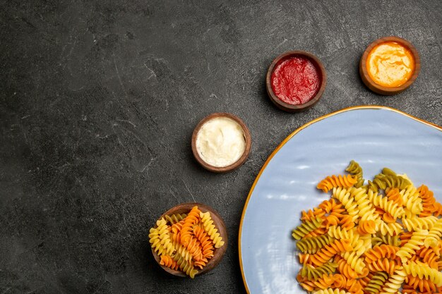 Vue de dessus de savoureuses pâtes italiennes pâtes en spirale cuites inhabituelles avec des assaisonnements sur le gris