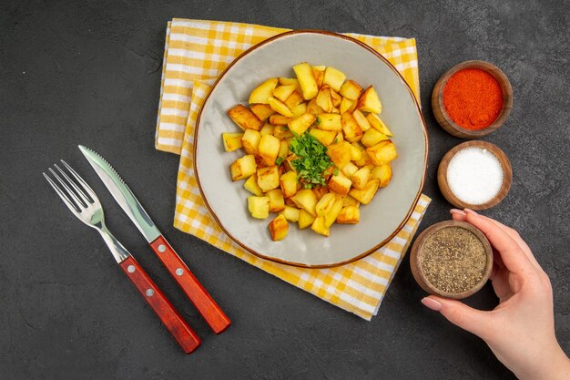 Vue de dessus de savoureuses pommes de terre frites à l'intérieur de la plaque avec des assaisonnements sur une surface gris foncé