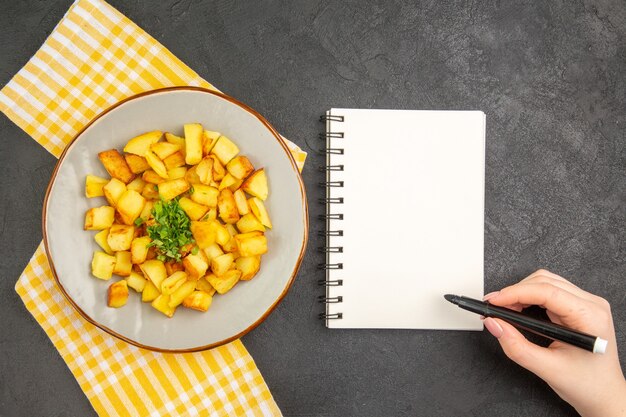 Vue de dessus de savoureuses pommes de terre frites à l'intérieur de la plaque avec bloc-notes sur une surface gris foncé