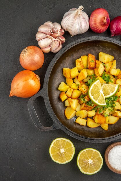 Photo gratuite vue de dessus de savoureuses pommes de terre frites à l'intérieur de la poêle avec des oignons et de l'ail autour sur la surface sombre