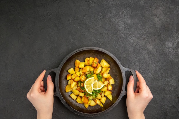 Vue de dessus de savoureuses pommes de terre frites à l'intérieur de la poêle avec des tranches de citron sur la surface sombre