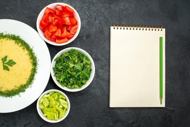 Vue de dessus de savoureuses purées de pommes de terre avec des légumes verts et des tranches de tomates fraîches sur fond gris