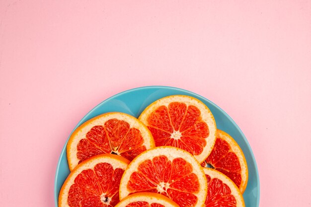 Vue de dessus de savoureuses tranches de fruits de pamplemousse à l'intérieur de la plaque sur la surface rose