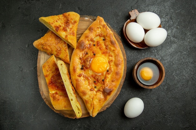 Vue de dessus savoureux pain aux oeufs cuit au four en tranches avec des oeufs frais sur le petit déjeuner de nourriture de pâte de pain de fond gris