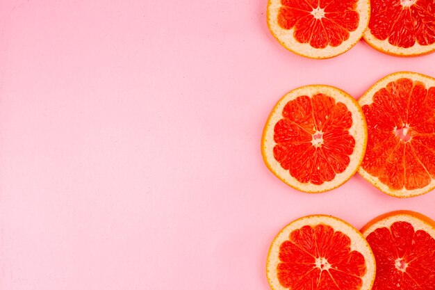 Vue de dessus de savoureux pamplemousses en tranches de fruits juteux sur une surface rose clair