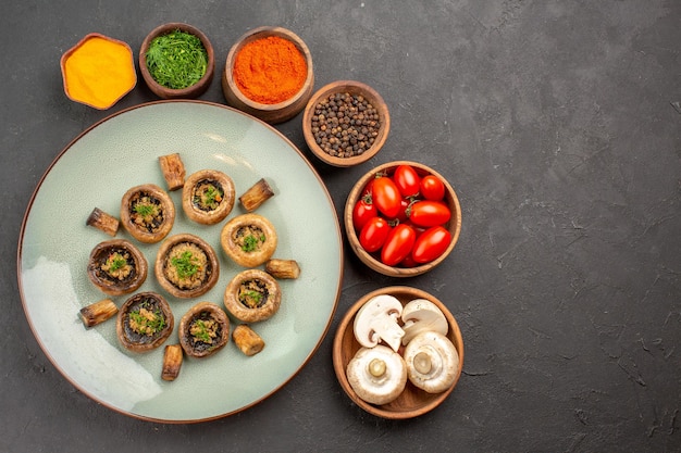 Vue de dessus savoureux repas de champignons avec tomates fraîches et assaisonnements sur le plat de surface sombre dîner repas cuisson champignon