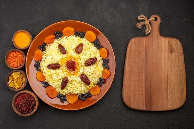 Photo gratuite vue de dessus savoureux repas oriental célèbre se compose de riz cuit et de différents raisins secs sur un bureau sombre