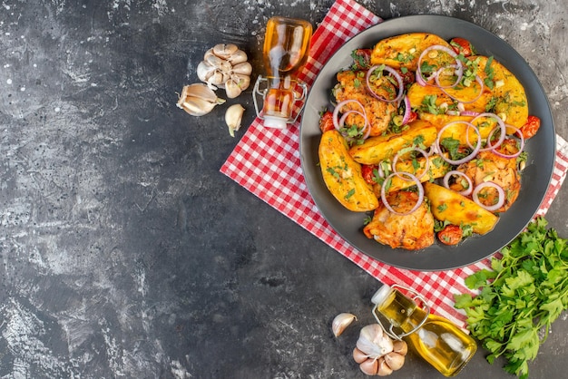 Vue de dessus d'un savoureux repas de poulet avec des pommes de terre et des légumes verts sur une serviette rouge dépouillée des bouteilles d'huile tombées sur le côté gauche sur une table de couleur sombre