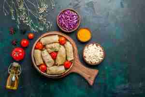 Photo gratuite vue de dessus savoureux repas de viande roulé avec du chou et des tomates appelé dolma avec de l'huile d'olive sur un bureau bleu foncé