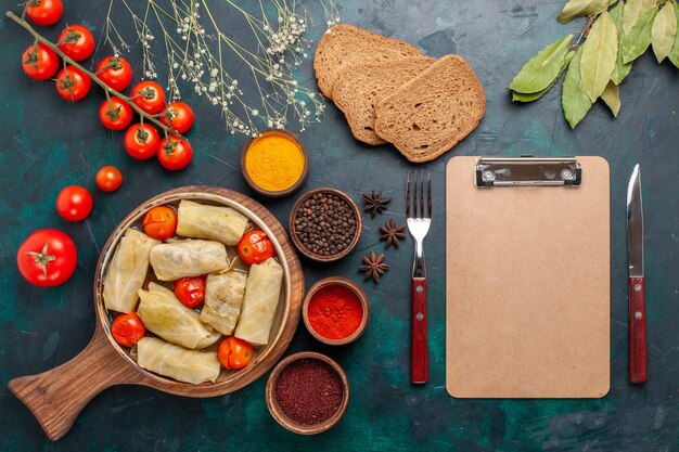 Vue de dessus savoureux repas de viande roulé à l'intérieur du chou avec du pain et des tomates fraîches sur le bureau bleu foncé