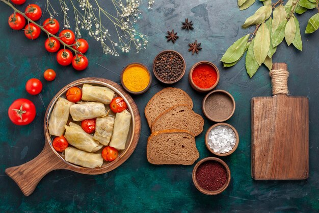 Vue de dessus savoureux repas de viande roulé à l'intérieur du chou avec du pain et des tomates fraîches sur le bureau bleu foncé