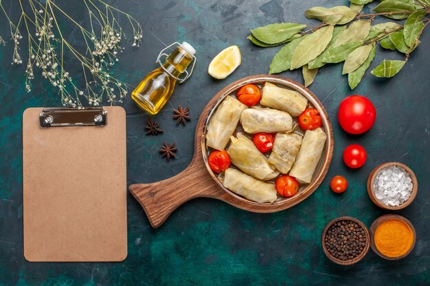 Vue de dessus savoureux repas de viande roulé à l'intérieur du chou avec de l'huile d'assaisonnement et des tomates fraîches sur le bureau bleu foncé