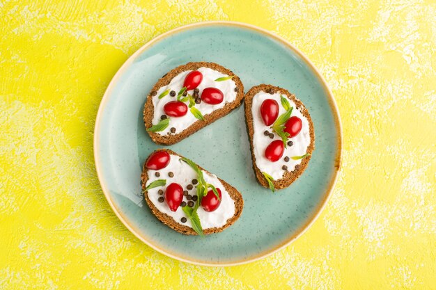 Vue de dessus de savoureux toasts de pain avec de la crème sure et des cornouillers sur la surface jaune