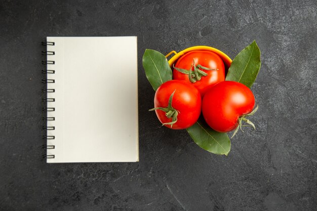 Vue de dessus un seau avec des tomates et des feuilles de laurier et un ordinateur portable sur un sol sombre