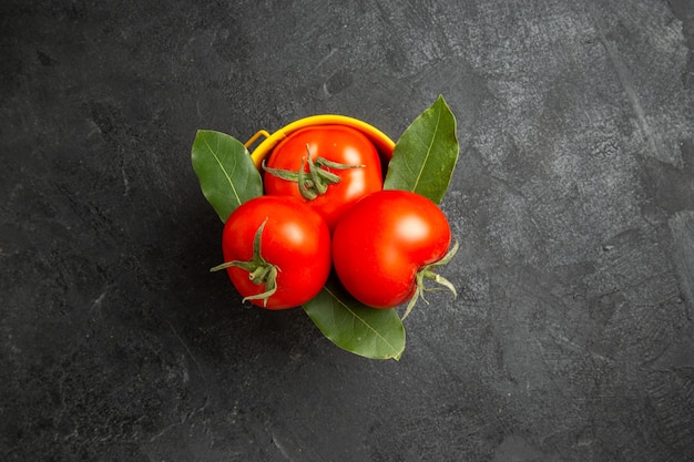 Vue de dessus un seau avec des tomates et des feuilles de laurier sur un sol sombre